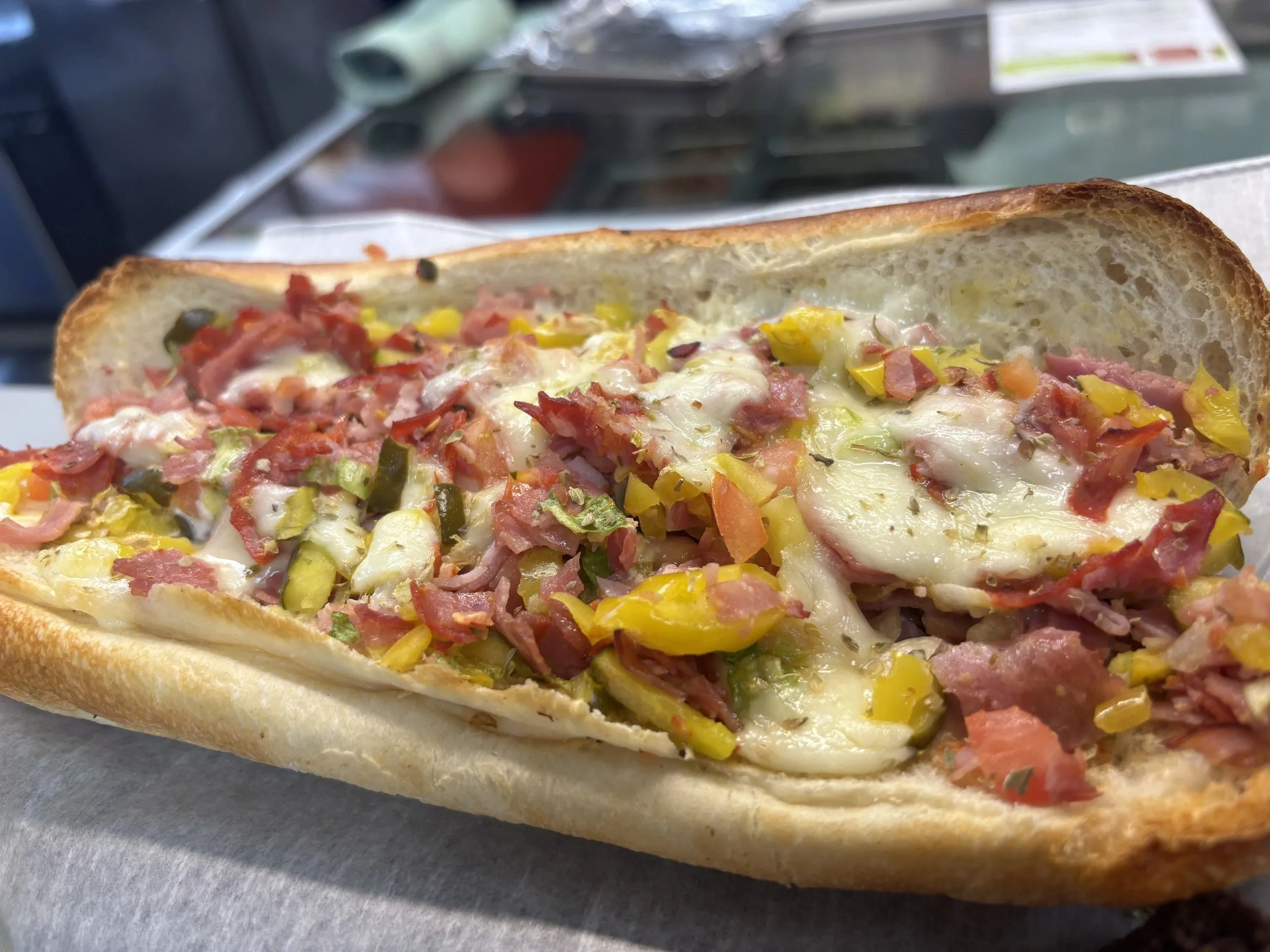 Italian sub piled with melted cheese, peppers, and cured meat